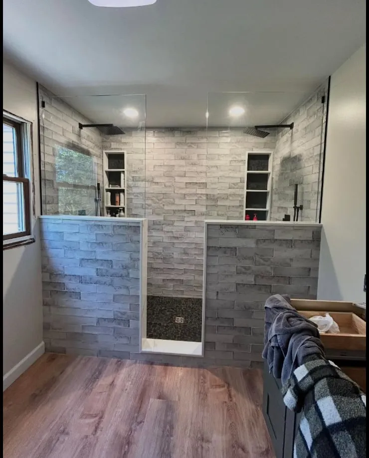 A double-entry 4×8 shower with dual rain heads, built-in niches and a pebble-stone floor — with new LVP flooring through the room.