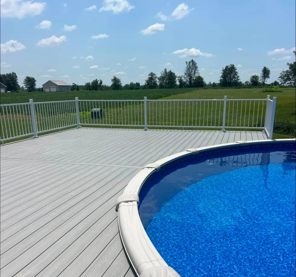 A low-maintenance composite pool deck with white aluminum railing, horizontal-slat skirting and wide stairs, wrapping an above-ground pool.